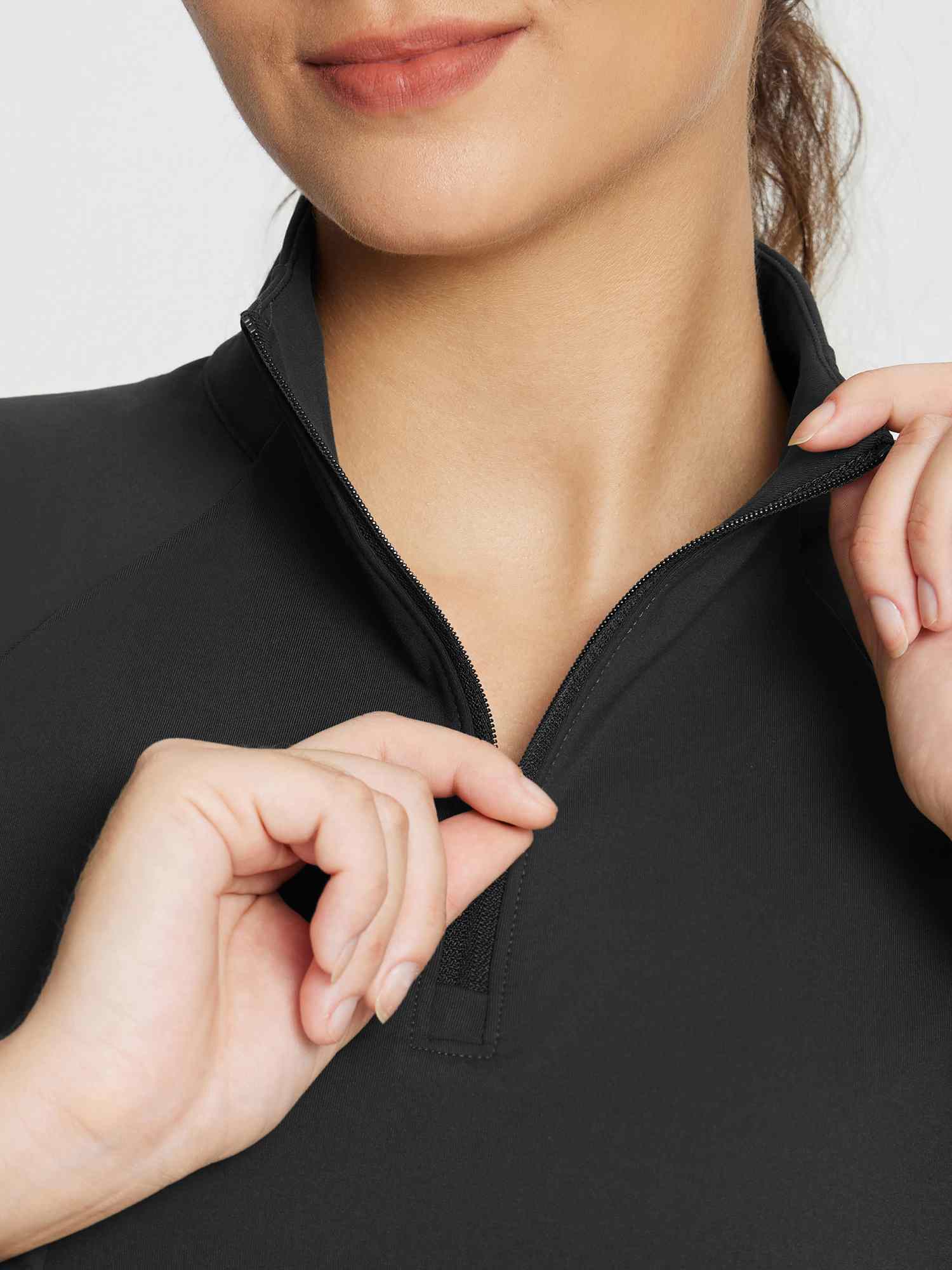 Close-up of a woman's hands zipping up the collar of a black outdoor fleece-lined knit dress. #color_Black