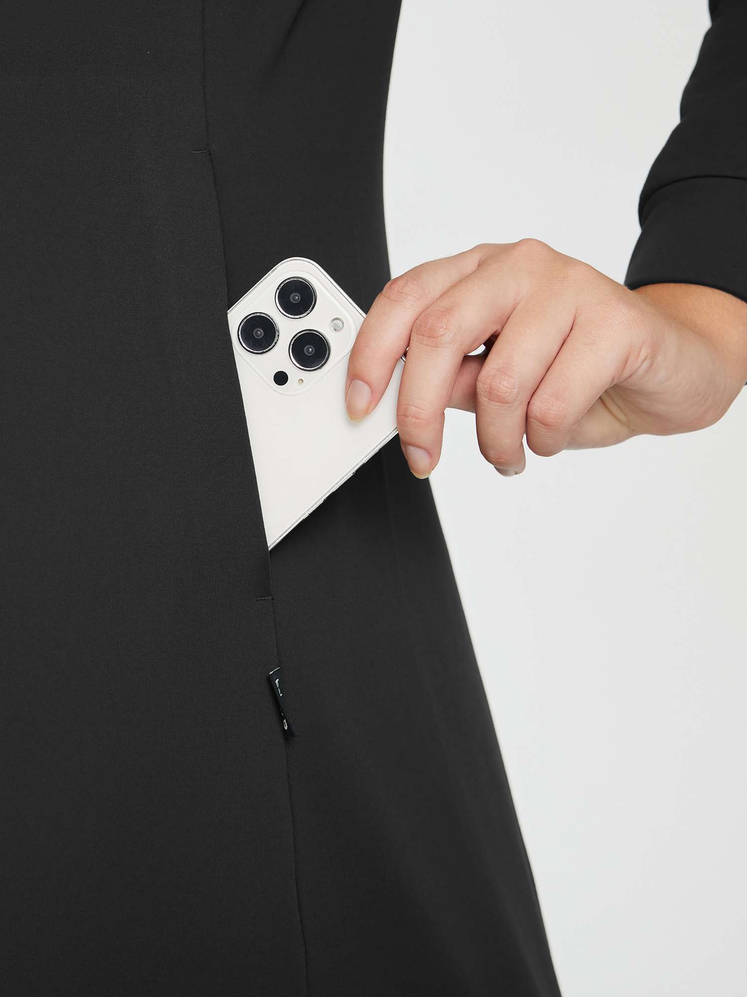 Close-up of a black outdoor fleece-lined knit dress with a hand placing a smartphone into a side pocket. #color_Black