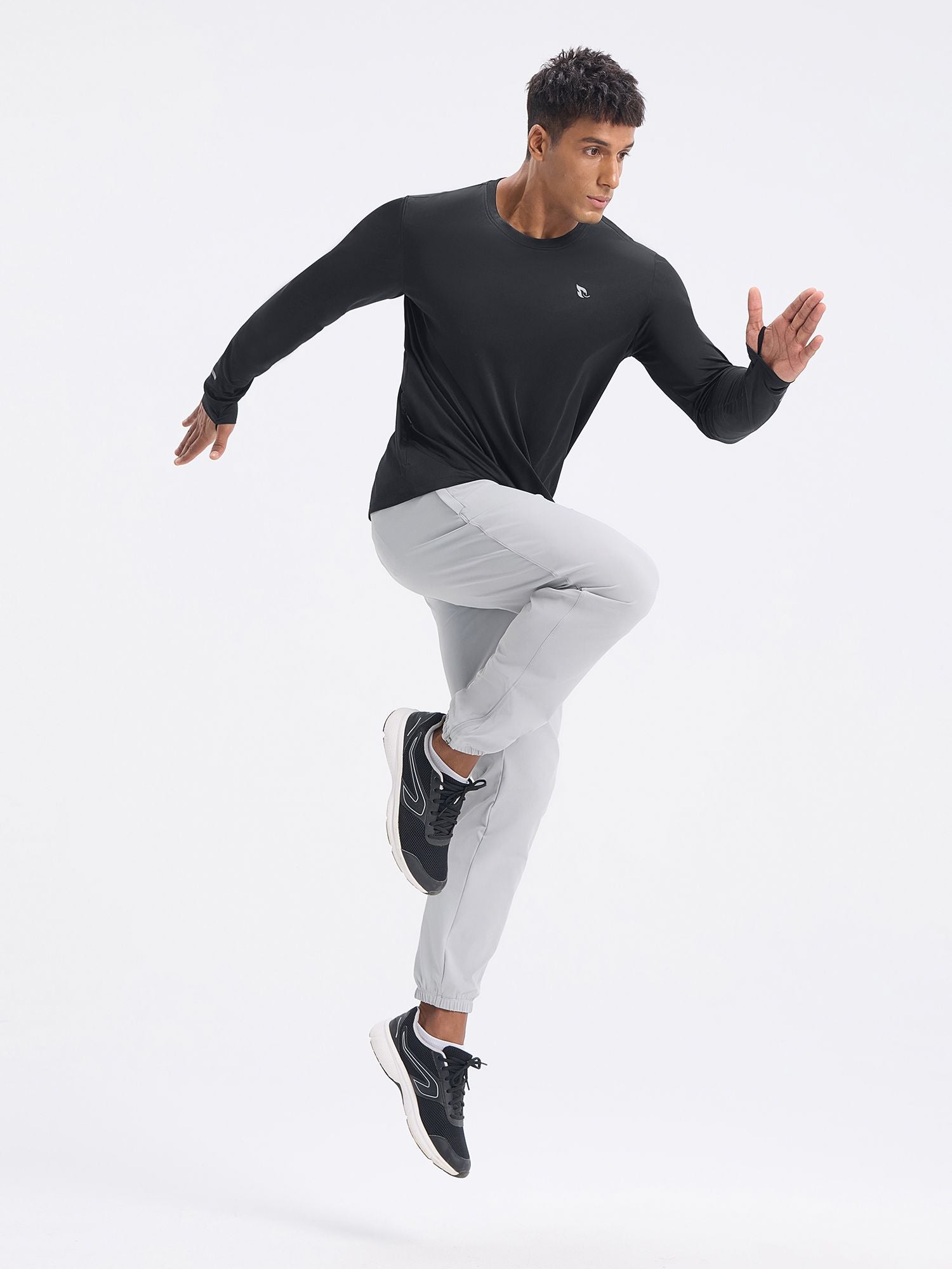 Man in black long sleeve cycling shirt and light grey pants with black sneakers jumping #color_Black