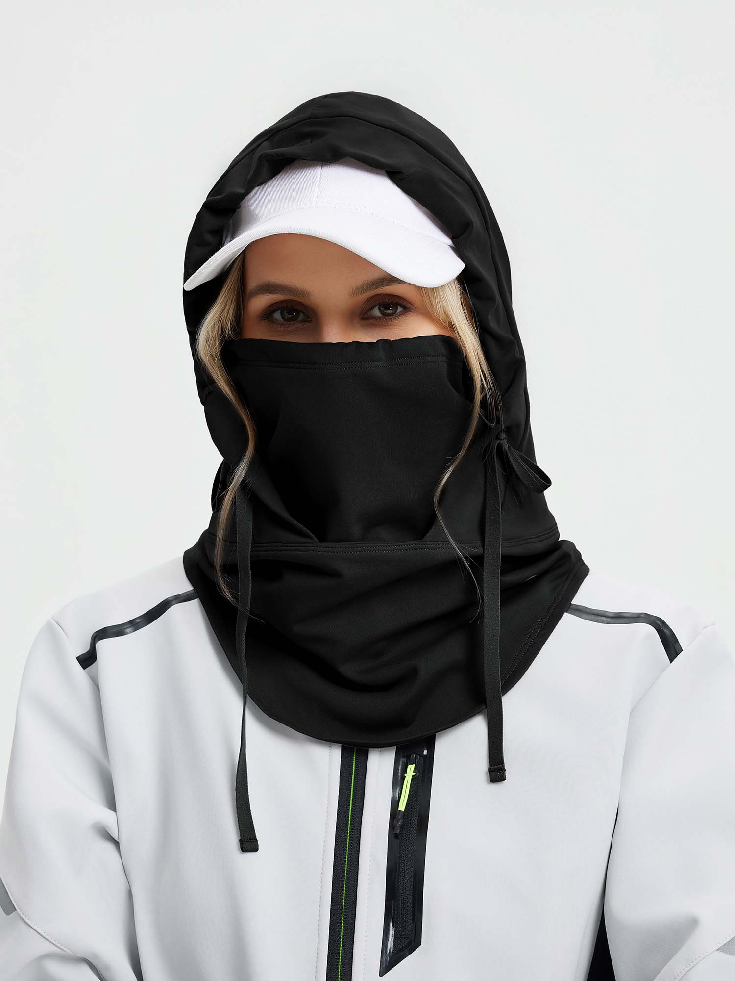 Woman in black ski hat with integrated face cover and white cap, under light gray waterproof jacket.