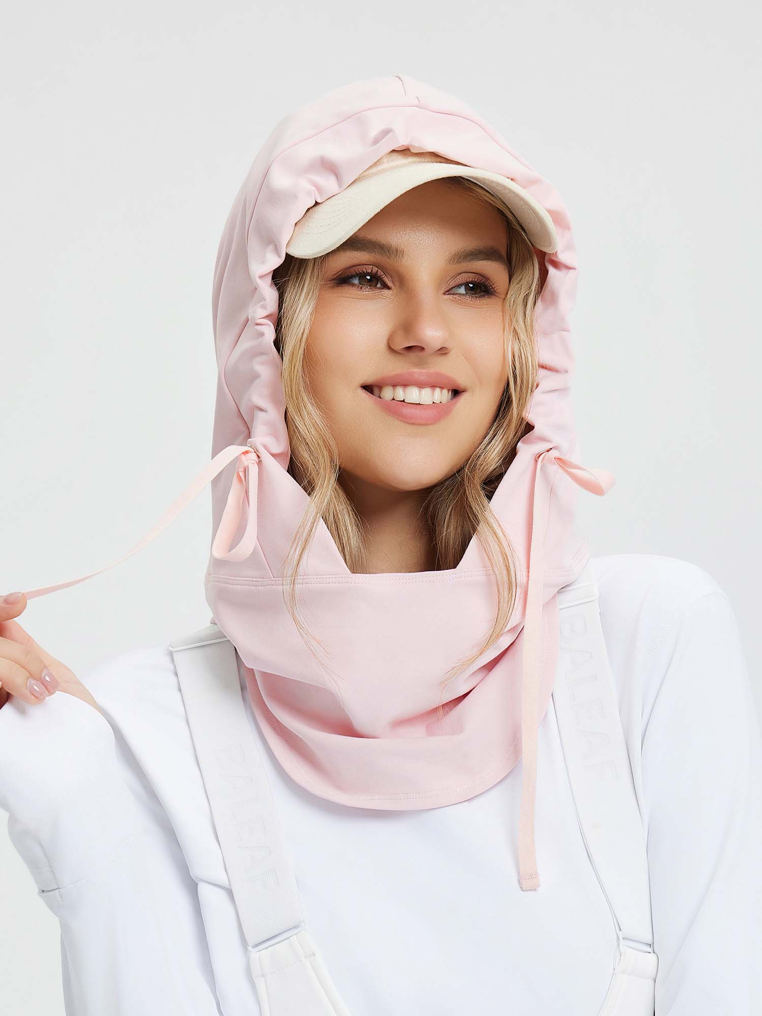 Unisex pink fleece-lined ski hat with adjustable ties and a cream baseball cap peeking out from underneath. #color_Light Pink