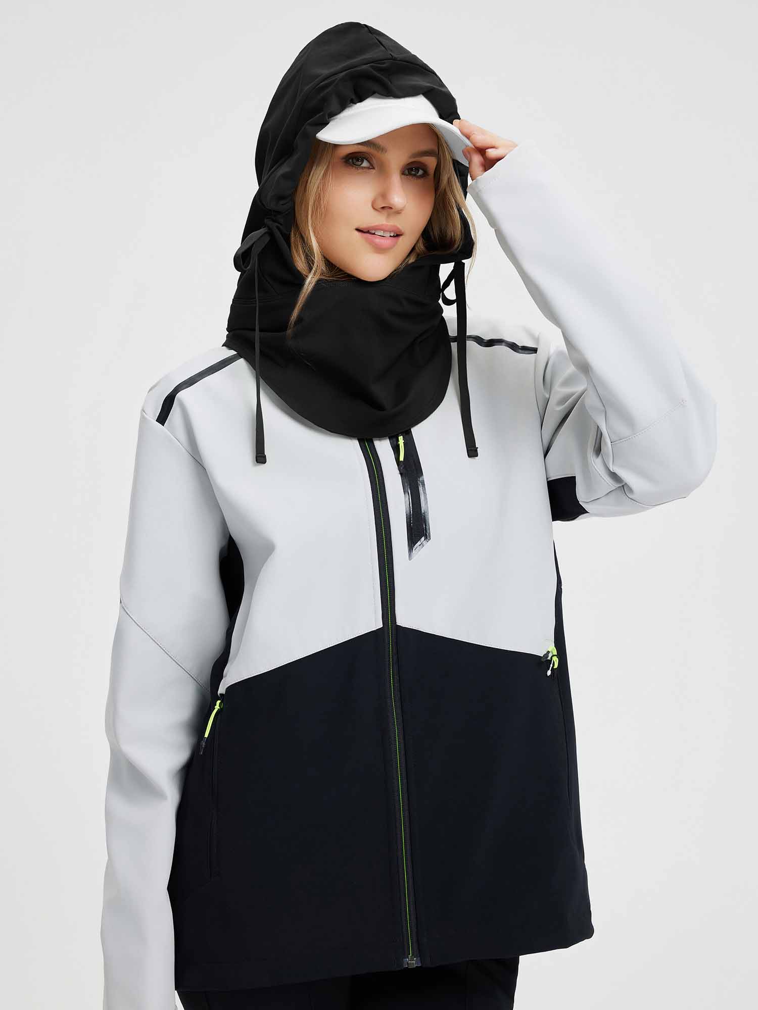 Woman wearing a grey and black ski jacket with a black hood and neck gaiter, a white cap underneath. #color_Black