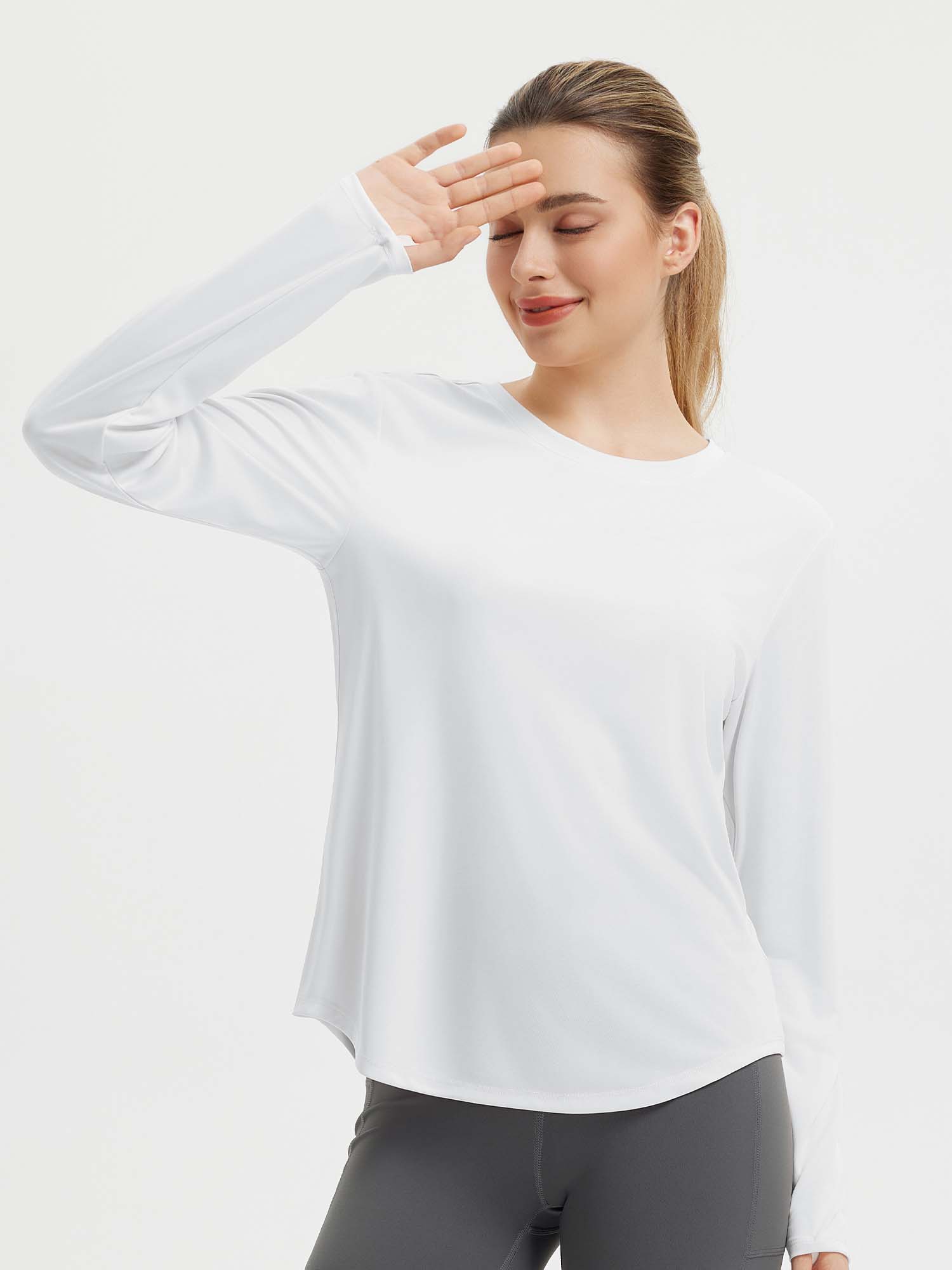 Woman wearing a white long sleeve running shirt with thumbholes, paired with grey leggings. #color_White