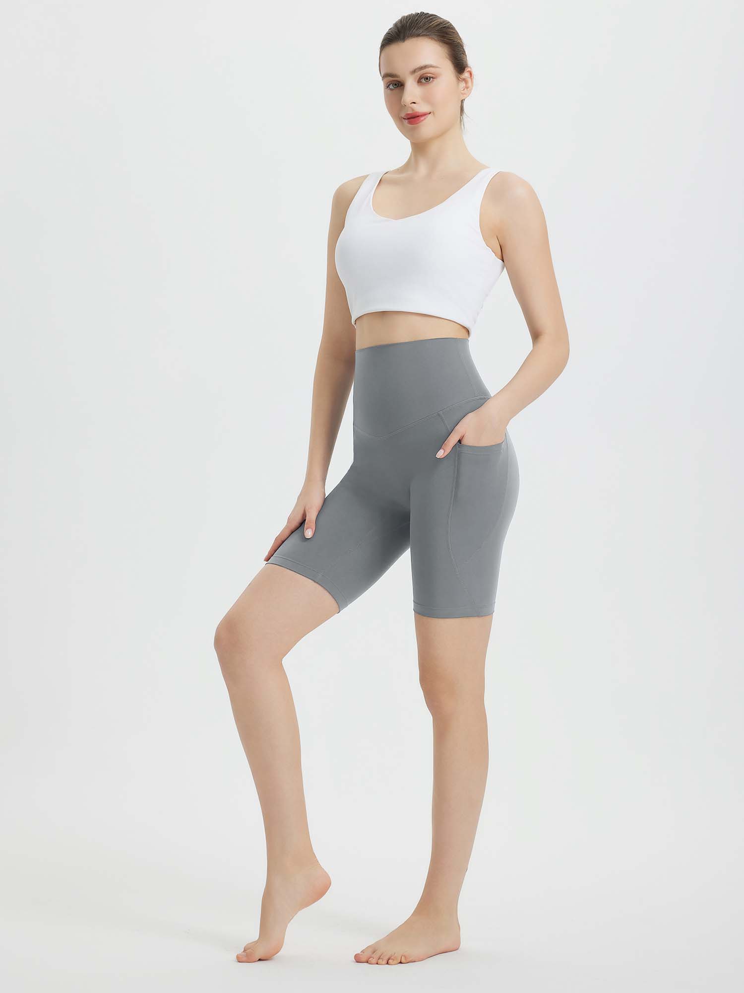 Woman wearing grey 8" super high-waisted biker shorts with pockets, paired with a white sports bra. #color_Dark Gray