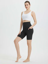Woman in black 8-inch biker shorts with high waist and side pockets, paired with a white sports bra. #color_Black