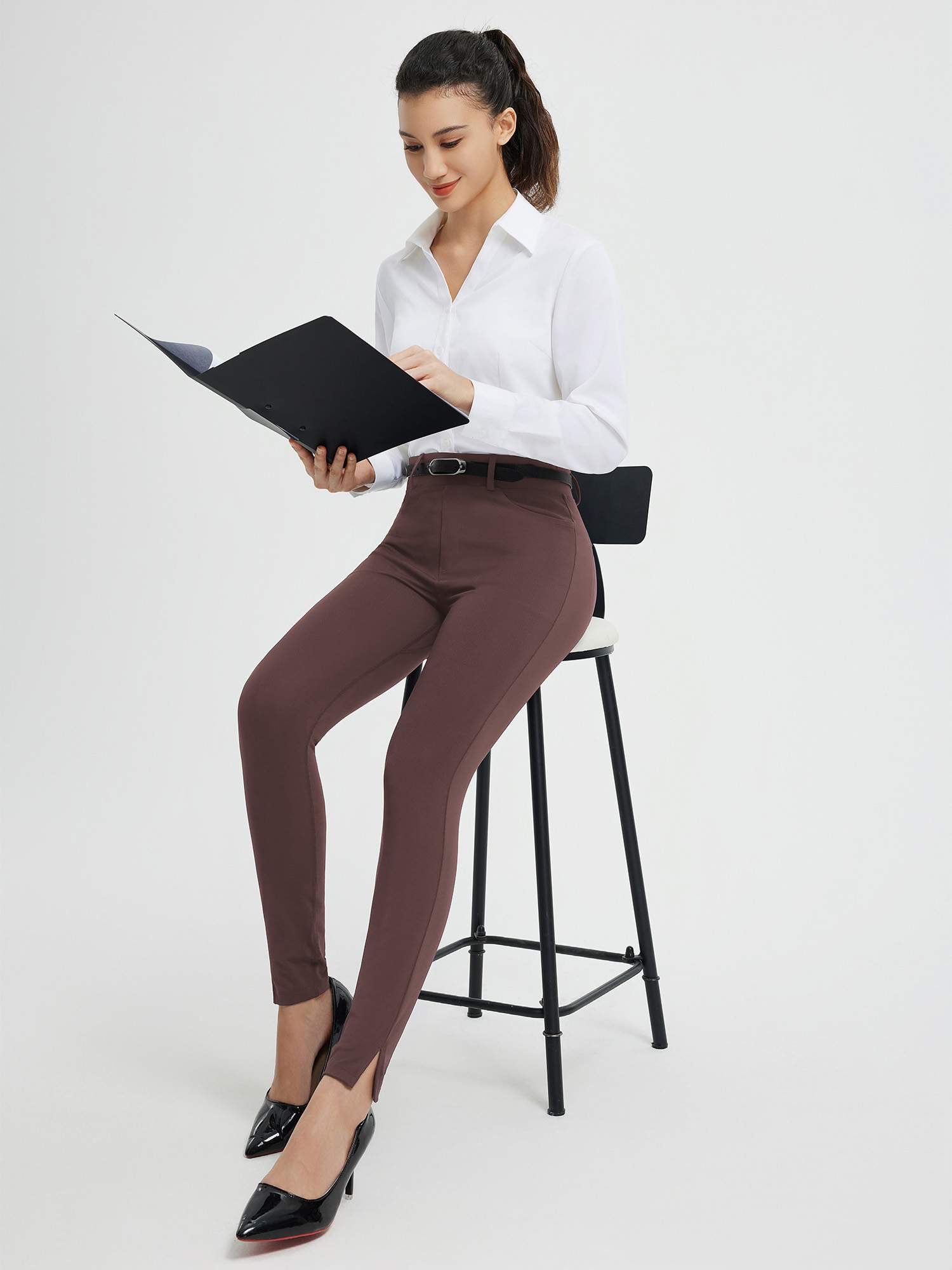 Woman in brown high-waisted yoga business pants and white shirt, holding a black folder. #color_Dark Brown
