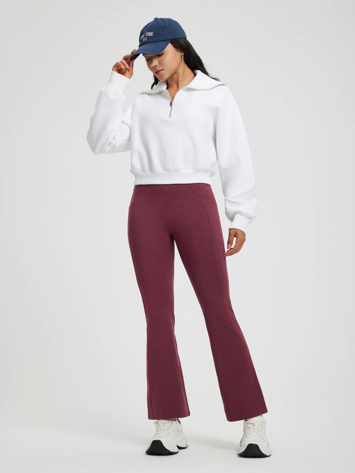 Woman in maroon floral fleece flare yoga pants and white zip-up sweatshirt, with NY cap. #color_Wine Red