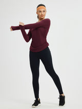 Maroon side-ruched long-sleeve yoga top with thumbholes and black leggings, worn by a woman stretching. #Color_Wine Red