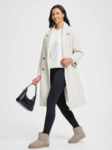 Woman wearing black thermal fleece yoga leggings, white sweater, and cream coat, carrying a black handbag. #color_Black