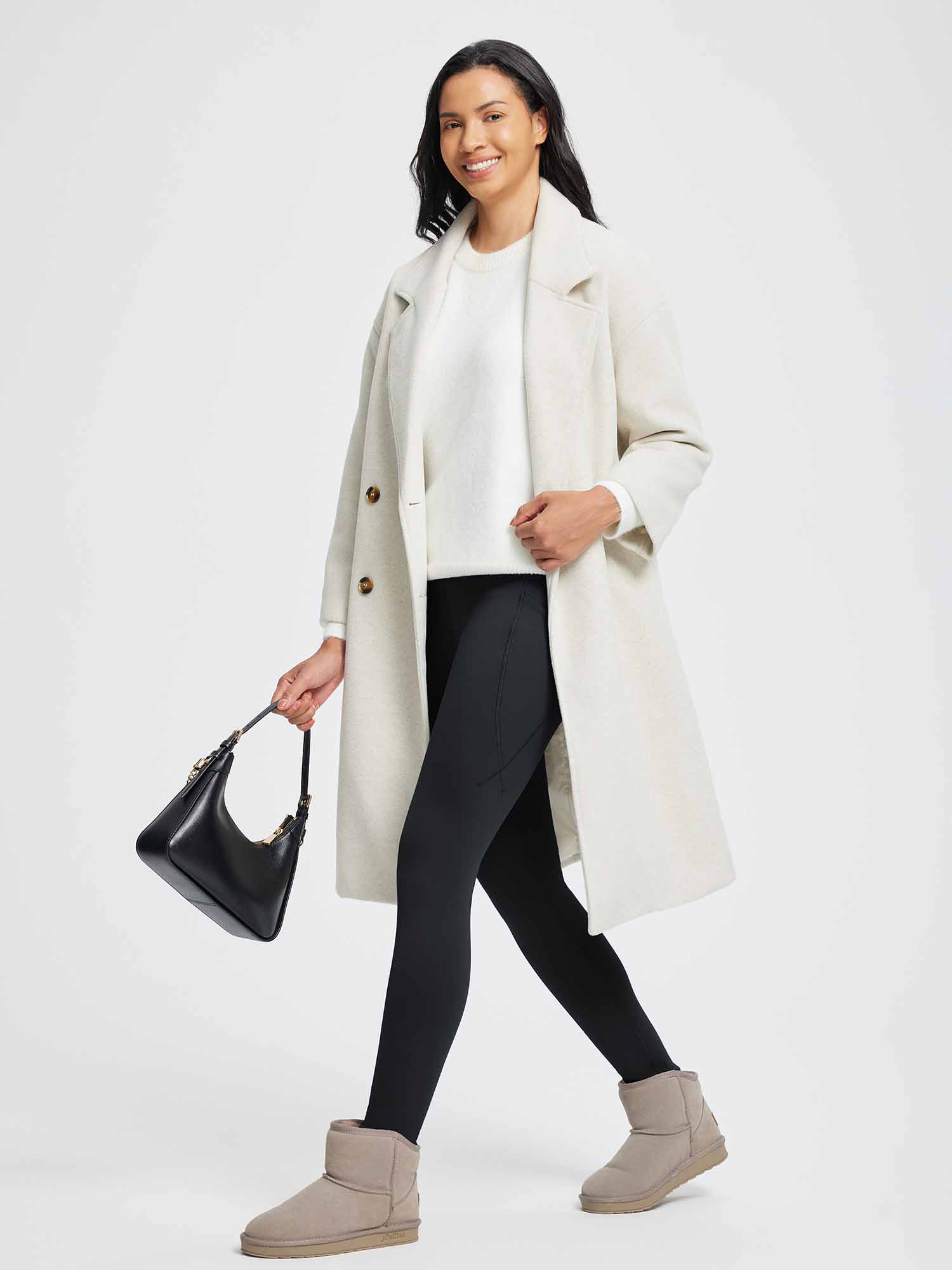 Woman wearing black thermal fleece yoga leggings, white sweater, and cream coat, carrying a black handbag. #color_Black