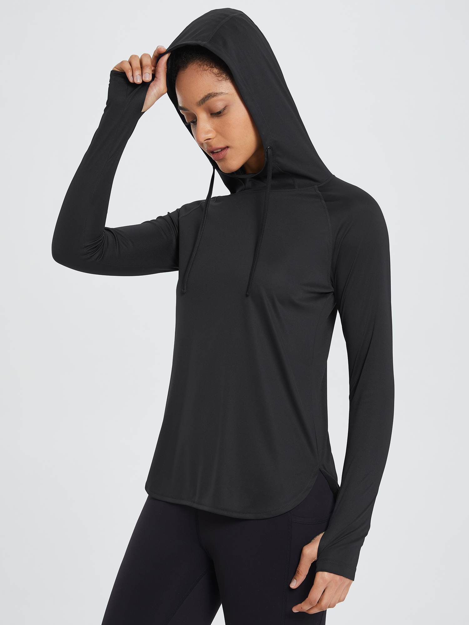 Black UPF 50+ sun hoodie shirt with thumbholes, worn by a woman in black leggings. #color_Black