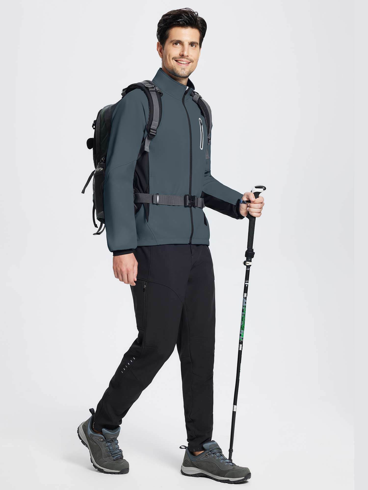 Man in dark gray thermal cycling jacket, black pants, and hiking shoes holding a trekking pole. #color_Dark Gray