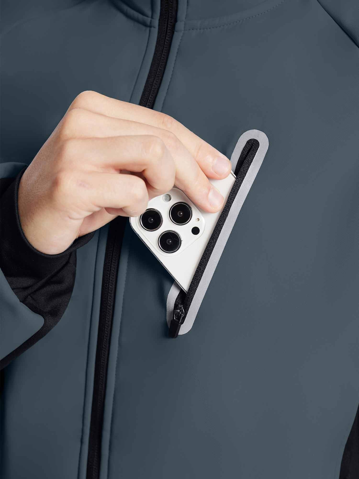 Man placing smartphone into zippered chest pocket of dark gray knit thermal cycling jacket. #color_Dark Gray