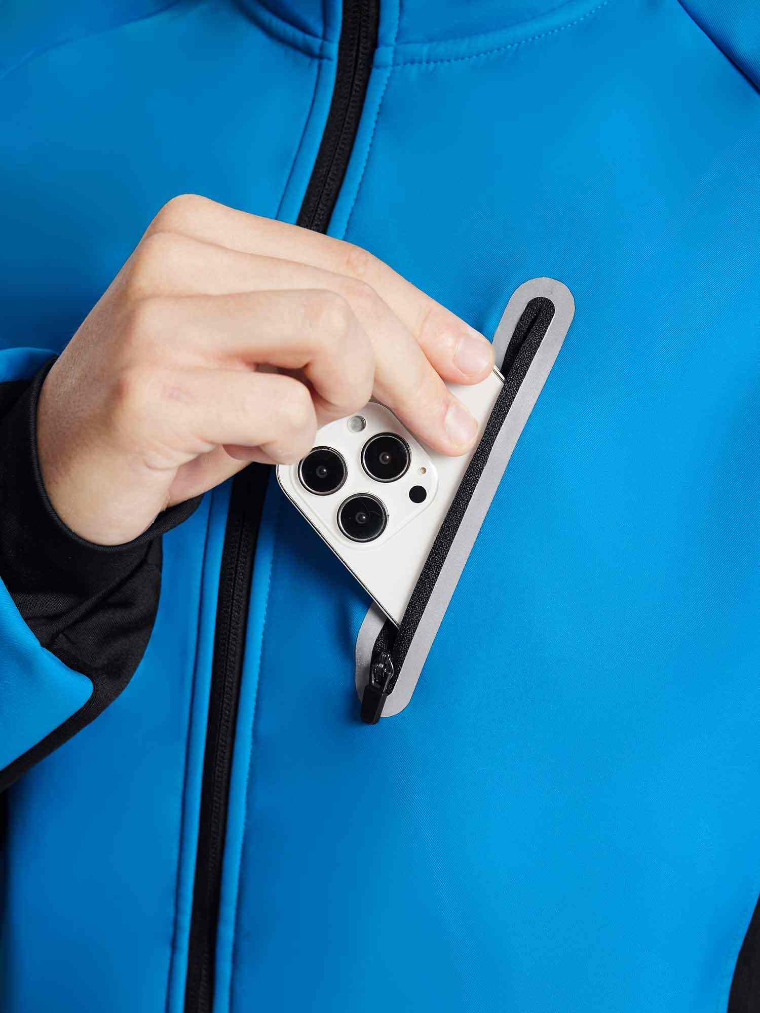 Man placing smartphone into zippered chest pocket of blue thermal cycling jacket. #color_Quartz Blue