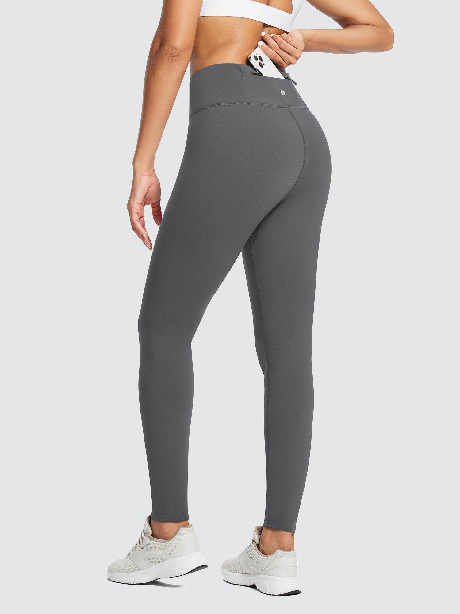 Woman wearing dark gray fleece-lined running leggings with a phone in the back zippered pocket. #color_Light Gray
