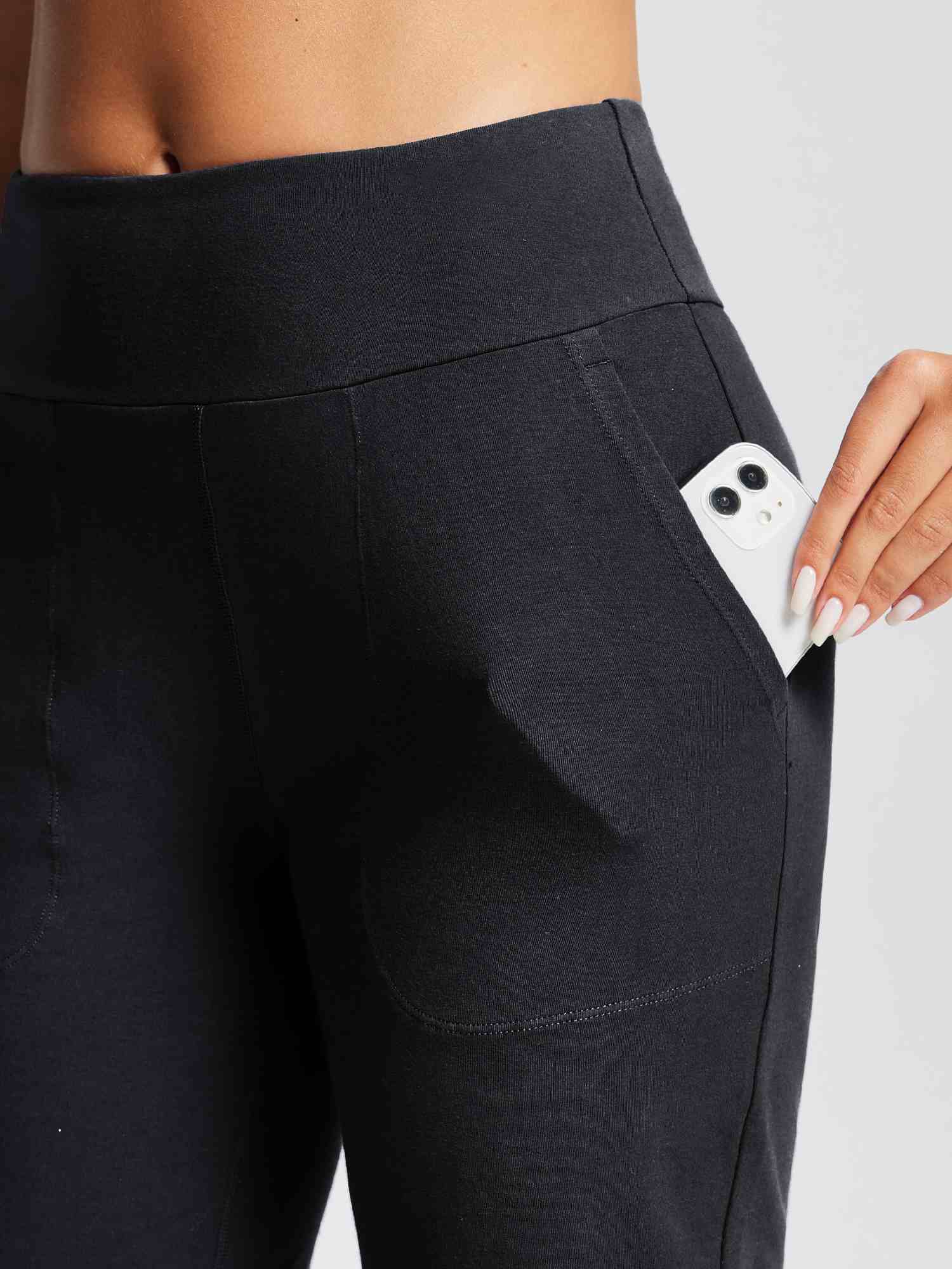 Close-up of black yoga shorts with a high knit waistband and a hand placing a smartphone into a side pocket. #color_Black