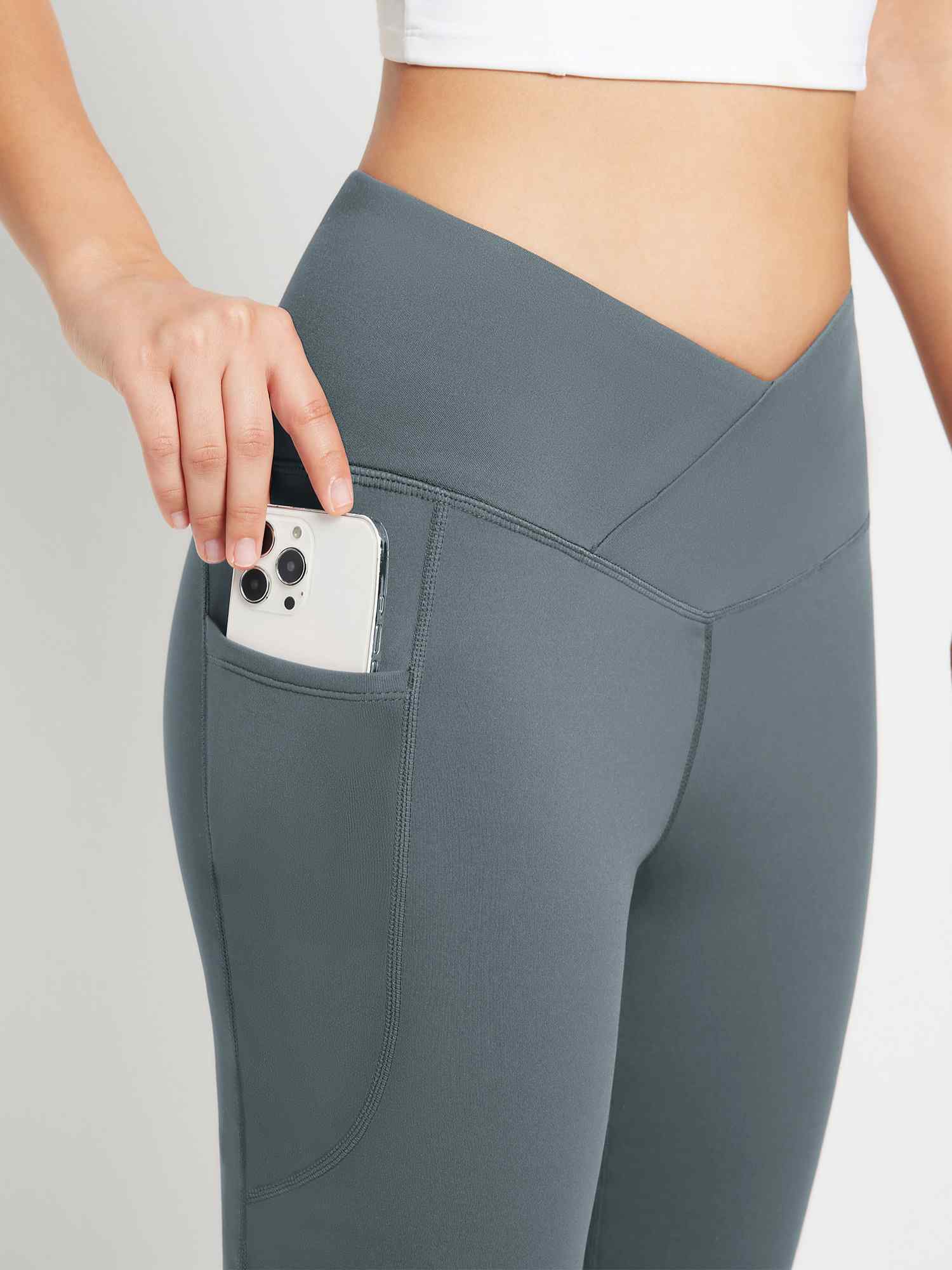 Woman placing phone in pocket of grey crossover waist fleece flare pants #color_Dark Gray