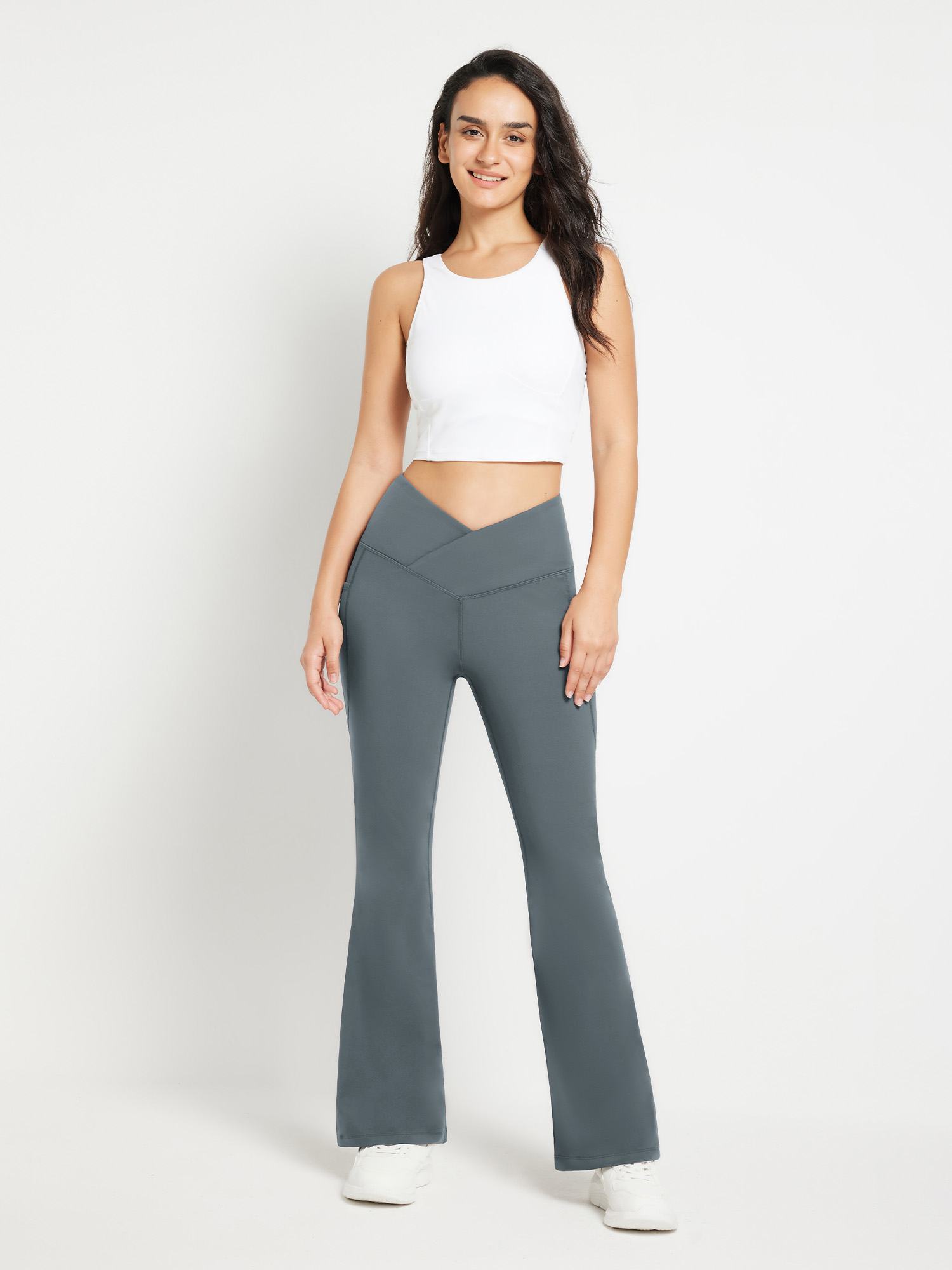 Woman wearing charcoal crossover waist fleece flare pants with pockets and white sneakers. #color_Dark Gray