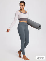 Woman in grey petite fleece-lined yoga leggings and a two-tone crop top holds a rolled yoga mat.