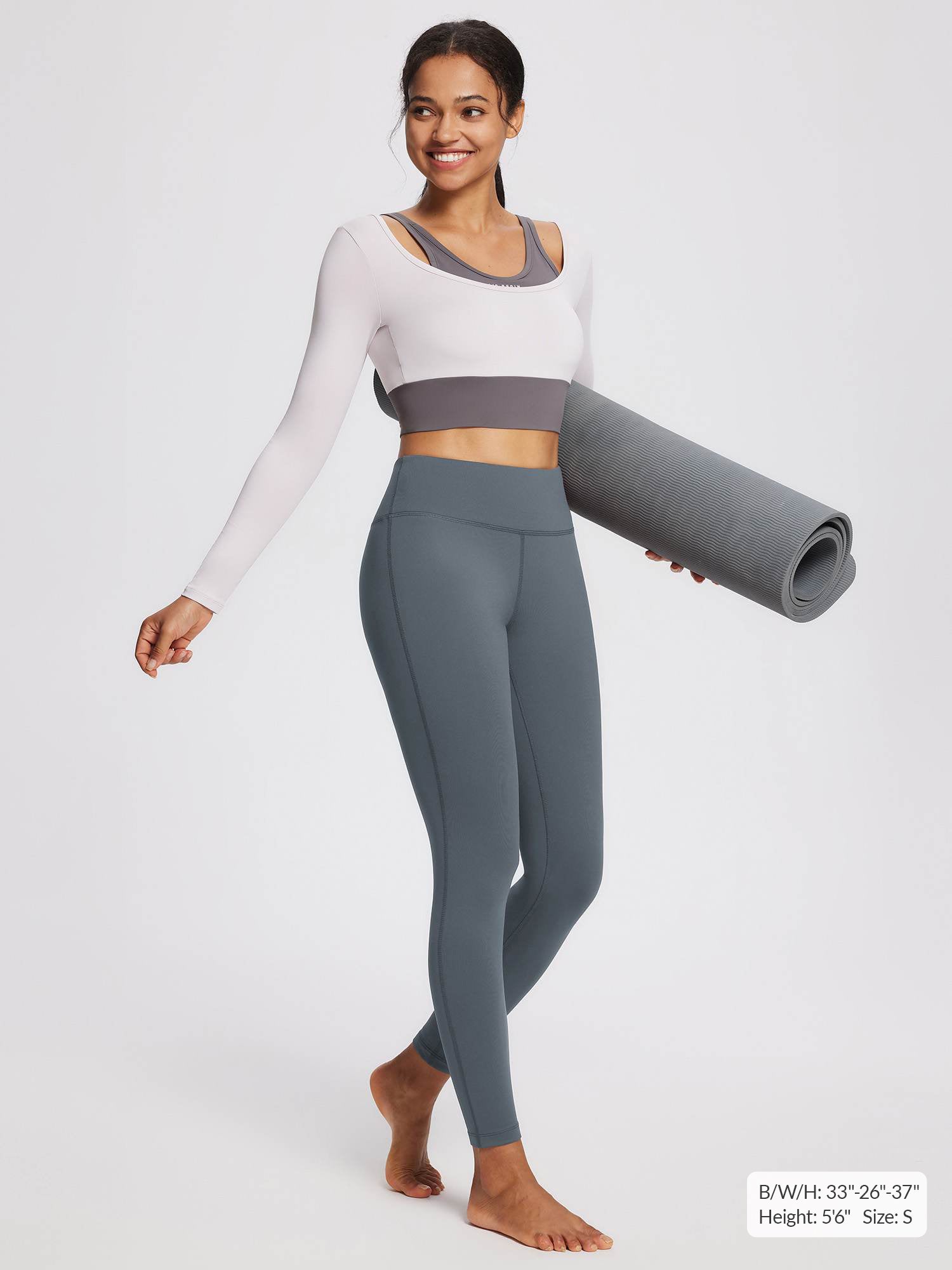 Woman in grey petite fleece-lined yoga leggings and a two-tone crop top holds a rolled yoga mat.