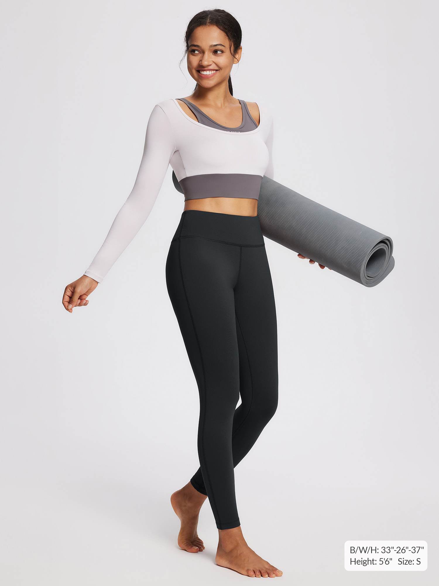 Woman in black fleece-lined yoga leggings and a long-sleeved top holding a yoga mat.