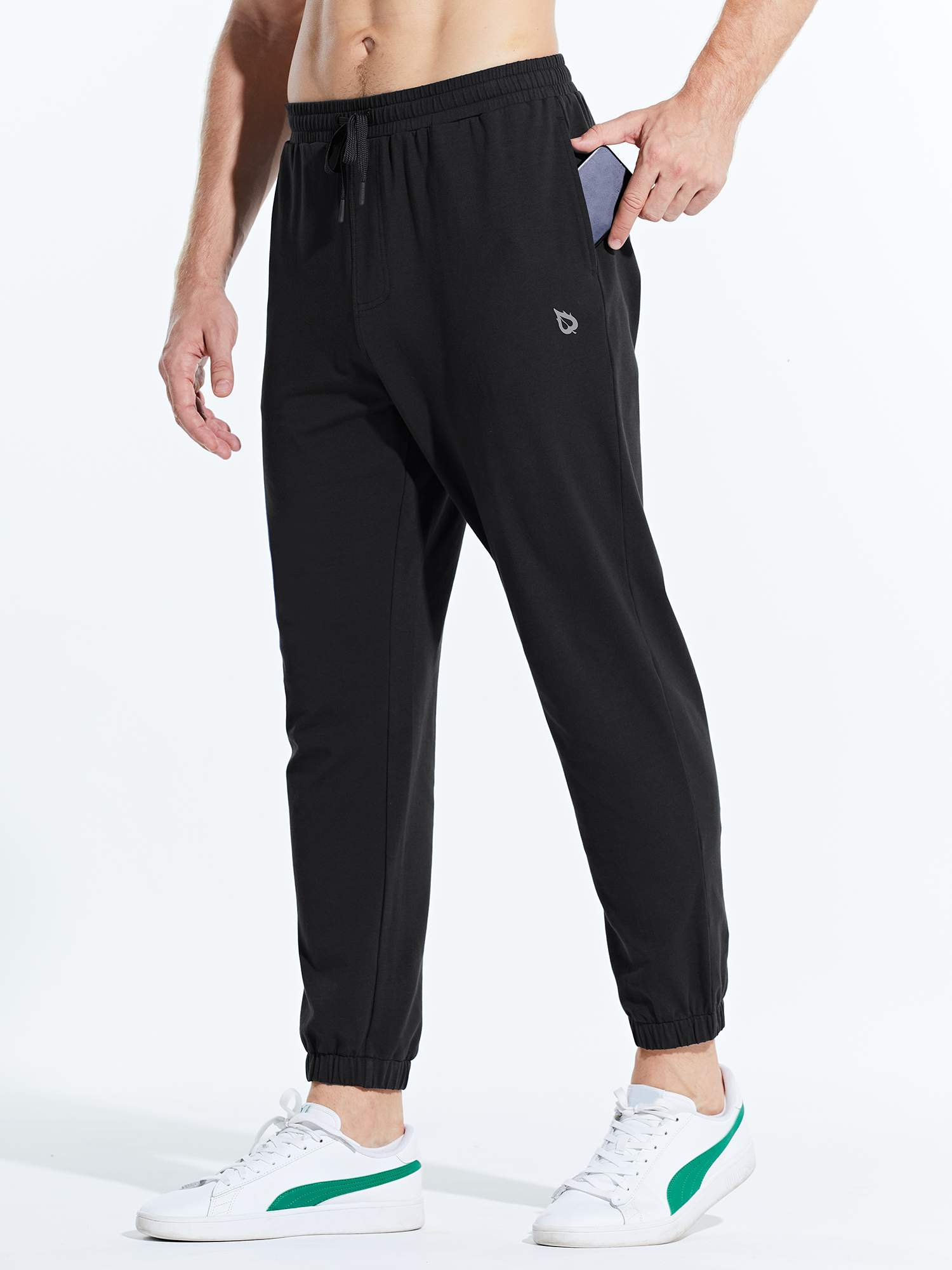 Men's black cotton joggers with phone pocket, drawstring, and cuffed ankles, paired with white sneakers. #color_Black/Blue