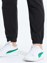Men's black cotton joggers with elastic cuffs and white sneakers with green stripe detail. #color_Black/Gray