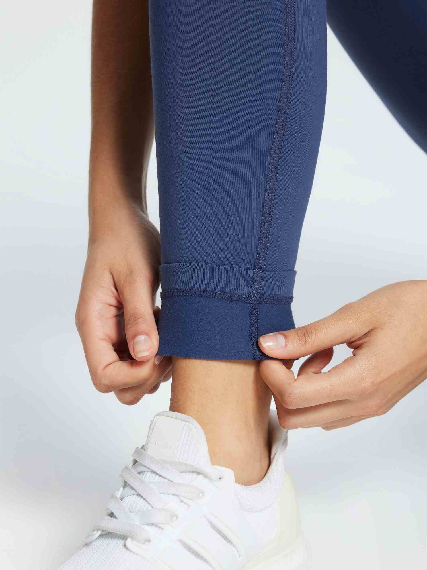 Close-up of navy blue 3/4 thermal ski leggings being adjusted at the ankle, paired with a white sneaker. #color_Navy Blue