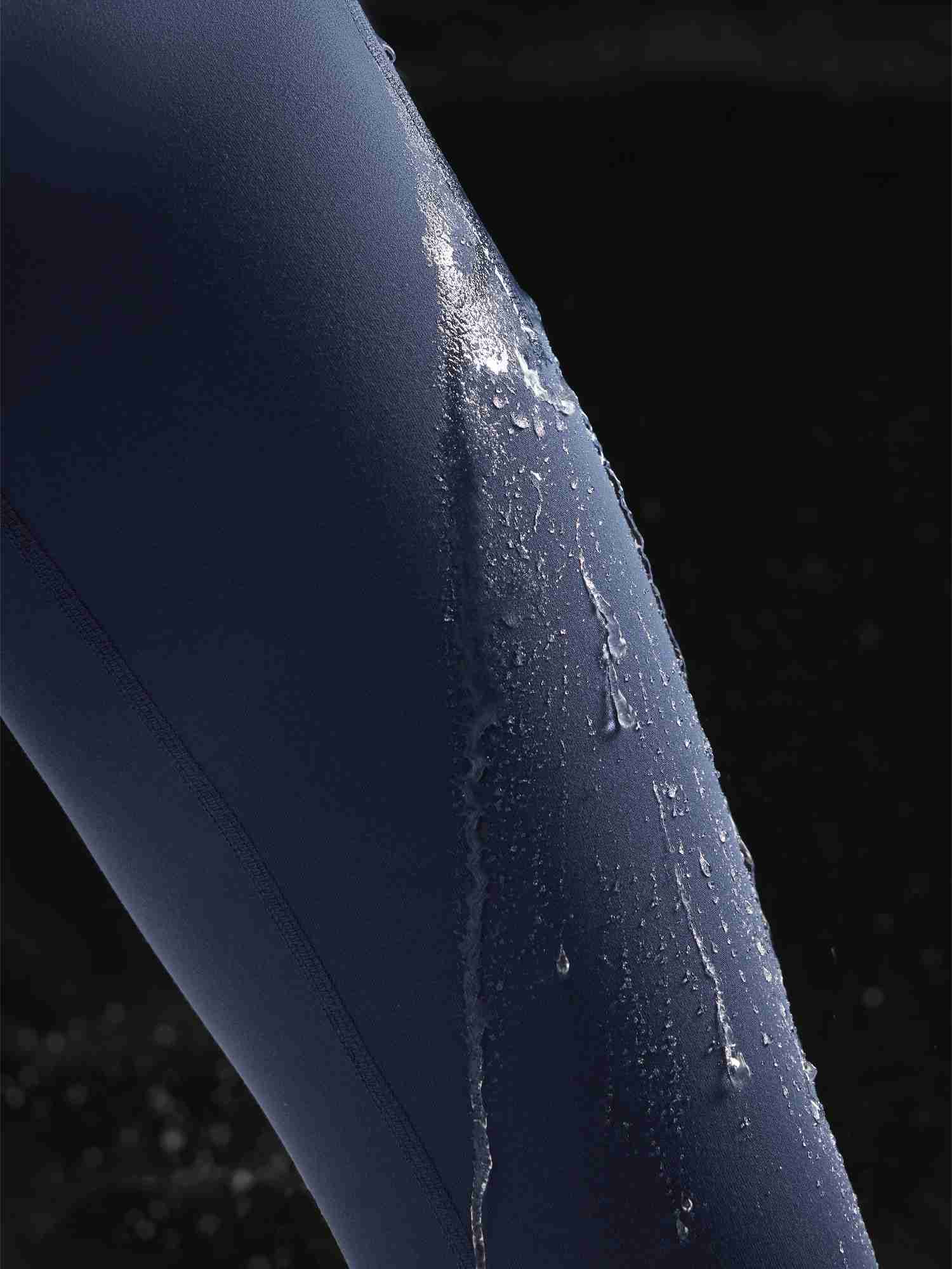 Close-up of navy blue water-resistant 3/4 thermal ski leggings with water droplets beading on the fabric. #color_Navy Blue