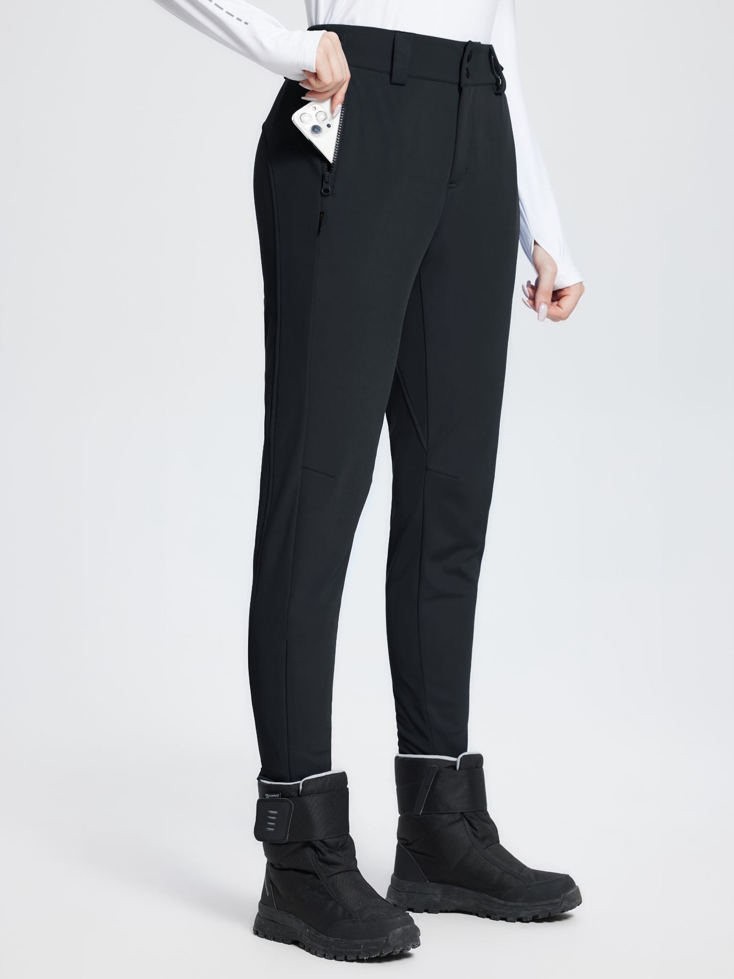Black stretch knit slim-fit ski pants with zippered pocket, worn by a woman with winter boots. #color_Black