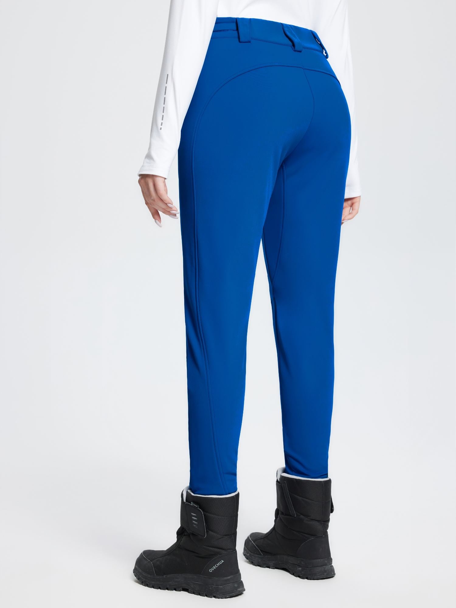 Woman wearing blue stretch knit slim-fit ski pants and a white long-sleeve shirt with black snow boots. #color_Quartz Blue