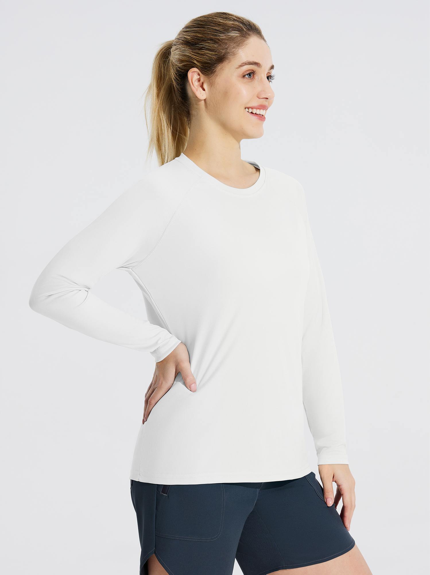 Woman wearing a white long sleeve rash guard and dark blue shorts, with her hand on her hip. #color_White