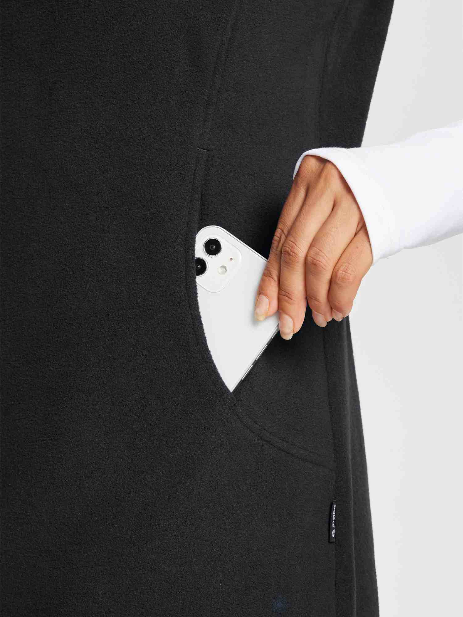 Black sleeveless fleece thermal dress with phone in pocket, worn over white long-sleeve shirt.
