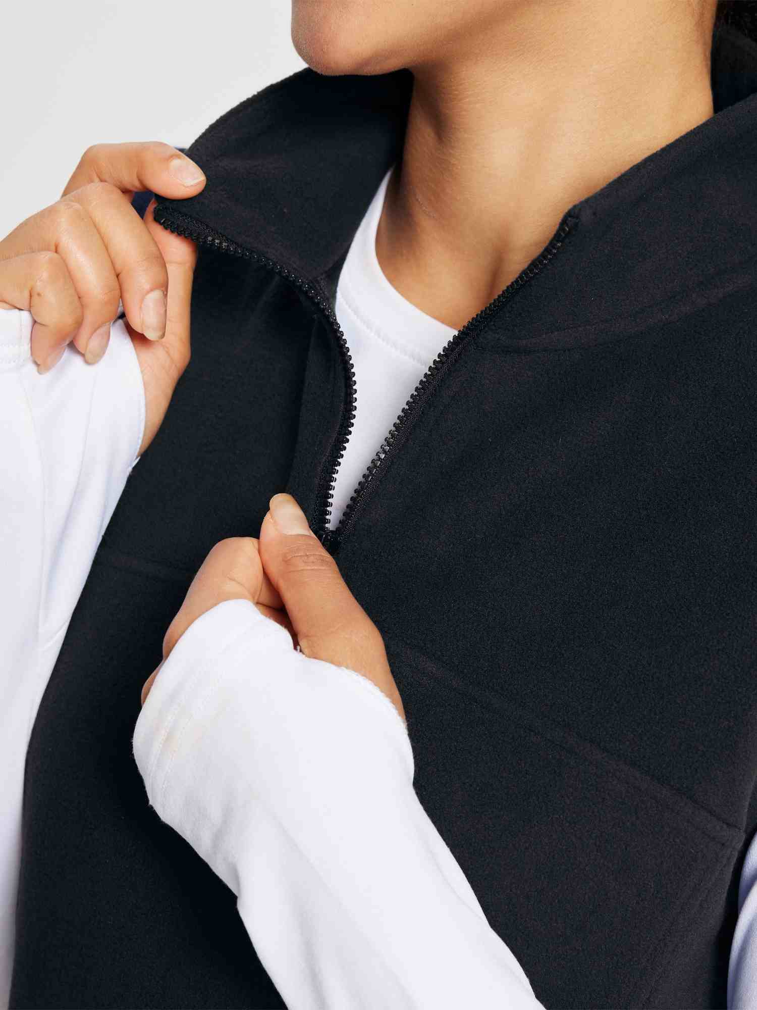Black sleeveless fleece thermal dress with quarter-zip collar, worn by a woman over a white long-sleeved shirt. #color_Black