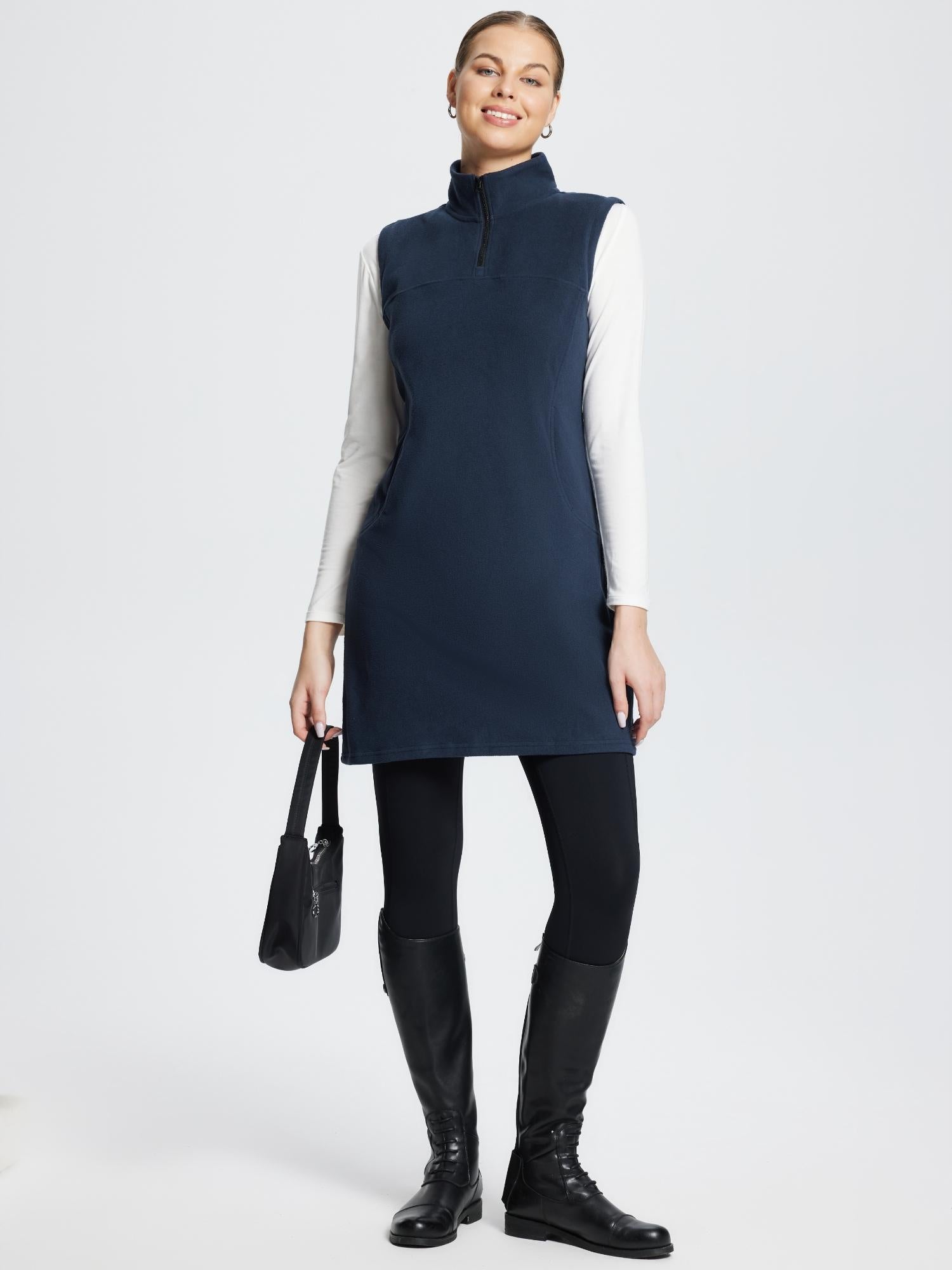 Navy blue sleeveless fleece thermal dress, quarter-zip, worn over white long-sleeve shirt, black leggings & boots.