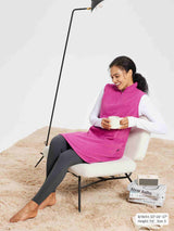 Woman in pink sleeveless fleece thermal dress and gray leggings holding a mug, sitting on a chair with a fluffy rug.